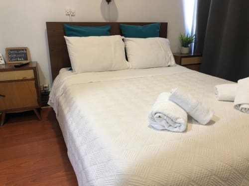 Quarto limpo da Guest House Infante Dom Henrique em Coimbra com roupa de cama creme, almofadas azul-petróleo, toalhas enroladas e