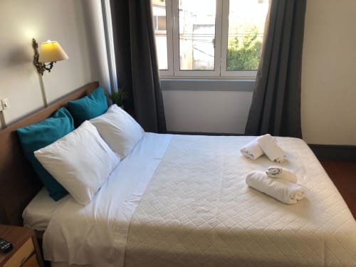 Quarto duplo da Guest House Infante Dom Henrique em Coimbra com roupa de cama branca, almofadas turquesas e janelas com vista para