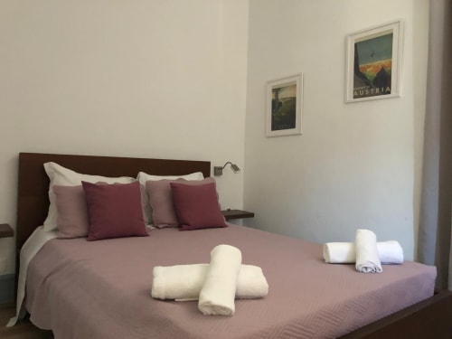 Quarto duplo deluxe na Pensão Infante Dom Henrique em Coimbra com roupa de cama malva, toalhas brancas e cartazes com vista da cidade