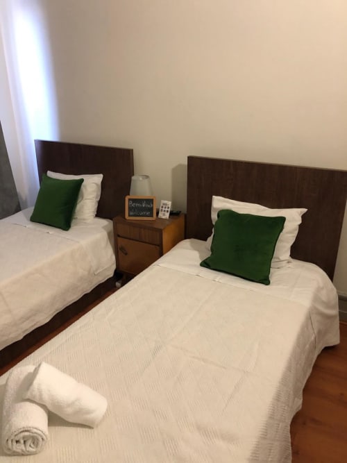 Quarto duplo na Pousada Infante Dom Henrique em Coimbra com camas brancas, almofadas verdes e cabeceiras em madeira escura