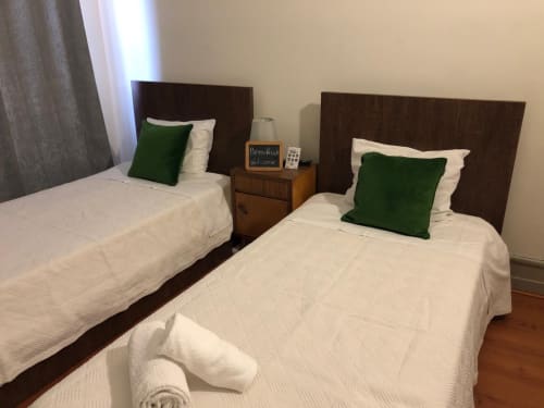 Quarto duplo na Guest House Infante Dom Henrique em Coimbra com camas brancas, almofadas verdes e cabeceiras em madeira escura