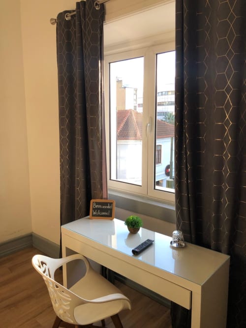 Moderna recepção de hotel com placa de boas-vindas, planta em vaso e controle remoto com vista para a cidade de Coimbra pelas janelas