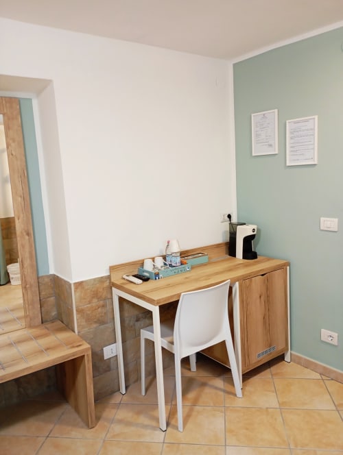 Area di lavoro in camera a Roccabianca Rooms, Stintino: scrivania in legno con sedia bianca, bottiglia d'acqua e macchinetta del caffè color acqua marina