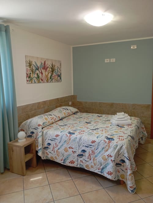 Camera luminosa alla Roccabianca B&B di Stintino con letto matrimoniale, biancheria floreale, comodino in legno e decorazioni tematiche marine