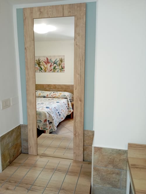 Ingresso della camera da letto a Roccabianca a Stintino con cornice in legno, specchio, letto floreale e pavimento piastrellato