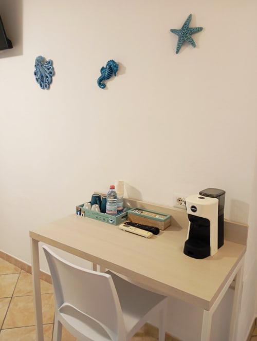 Scrivania in legno chiaro con sedia bianca, decorazioni murali blu con stelle marine e cavalluccio marino alle Roccabianca Rooms, Stintino