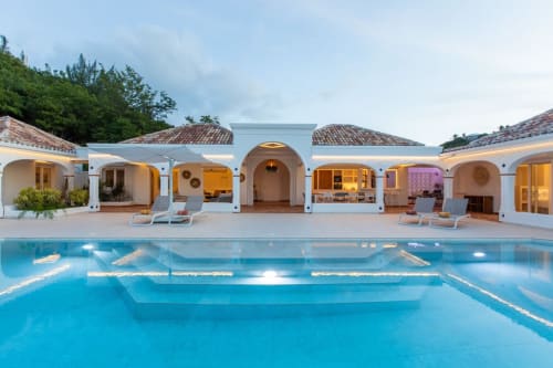 La piscine de prestige de Villa Agama et son architecture méditerranéenne blanche à Saint-Martin, avec transats et éclairage du soir
