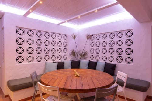 Salle à manger moderne à Villa Agama avec éclairage rose, table ronde en bois, panneaux muraux géométriques et sièges confortables