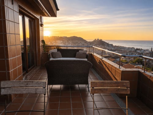 Vista al atardecer del mar desde el balcón del apartamento Holibai Baiona con silla de mimbre hacia la costa atlántica