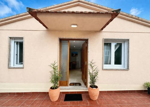 Casa rural color crema Laranxeira en Nigrán con patio de barro cocido, puerta de madera, plantas en macetas y vistas al mar