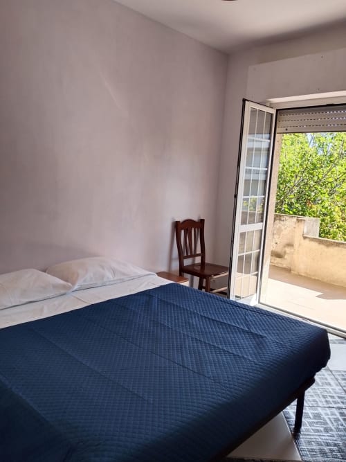 Camera da letto luminosa con balcone vista mare a Tales of Abruzzo, Atessa. Letto matrimoniale con coperta blu scuro, cuscini bianchi, in legno