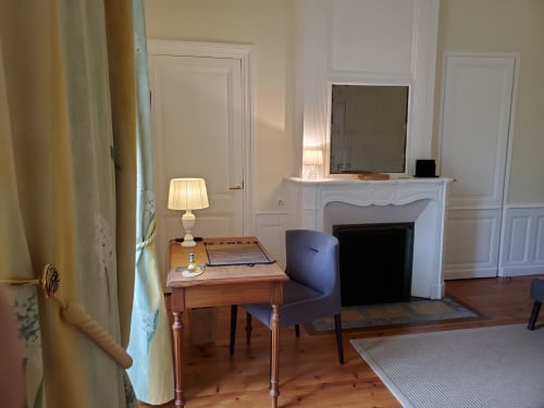 Chambre historique du Logis des Tourelles à Cognac avec cheminée, bureau en bois, fauteuil violet et mobilier d'époque