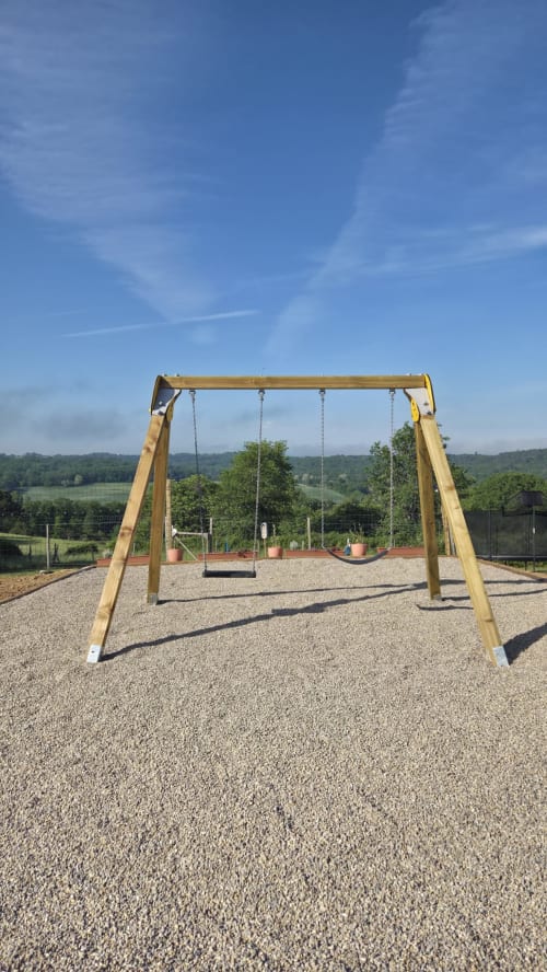 Houten schommelrek op grind op een zonnig speelplein met uitzicht op het Franse platteland bij Home Sweet Lodge Glamping
