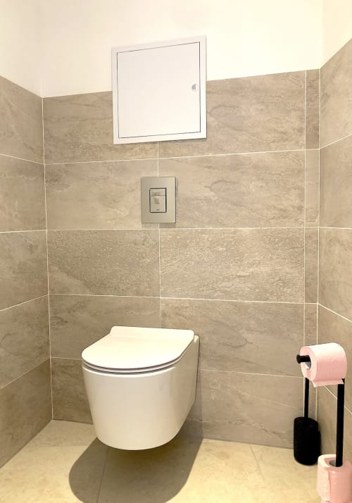 Baño moderno con inodoro blanco, azulejos beige, gabinete espejo y toallero rosa en Au Château De Villelongue