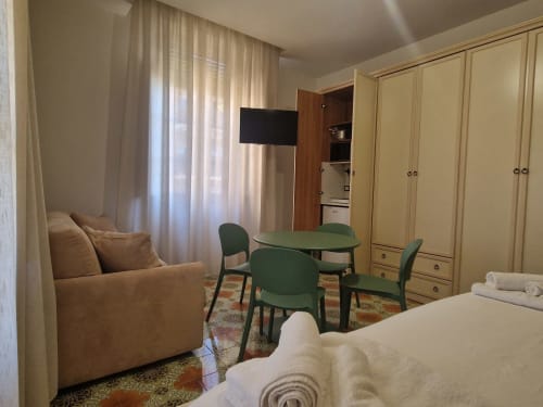 Camera spaziosa all'Il 900 B&B ad Avezzano con letto, poltrona marrone, tavolo verde, TV, guardaroba e vista sul giardino