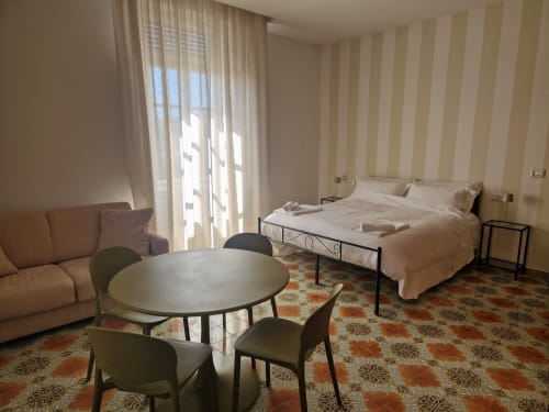 Camera dell'Hotel Il 900 Avezzano con letto, divano, tavolo rotondo, carta da parati rigata e vista giardino