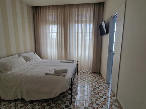 Camera luminosa all'Il 900 di Avezzano con letto bianco, tende trasparenti, TV e pavimento in piastrelle decorate