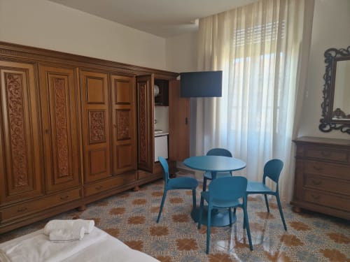 Camera Avventura all'Il 900 B&B di Avezzano: sedie blu attorno al tavolo da pranzo, armadio in legno, vista sul giardino con tende.