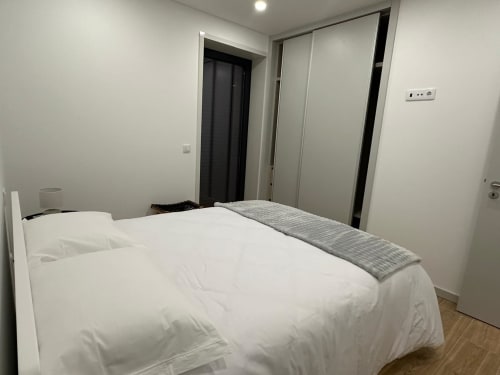 Quarto moderno com cama branca, passadeira cinzenta, guarda-roupa e porta preta na MiraReal GuestHouse em Macieira da Lixa