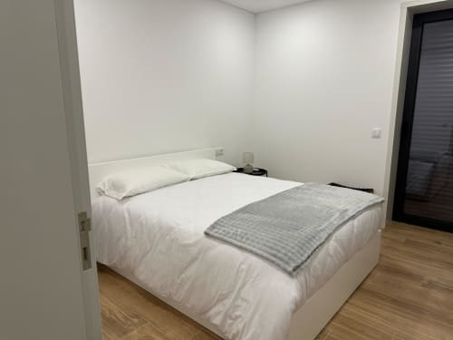 Quarto luminoso na MiraReal GuestHouse com cama branca, manta cinzenta e piso em madeira em Macieira da Lixa