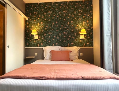 Chambre douillette aux Maisons Delphine avec papier peint fleuri, appliques chaleureuses et literie corail