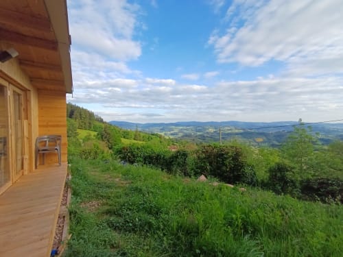 Wooden cabin balcony with mountain valley views, green landscape, and distant hills at La Maison de Dun in Saint Racho,