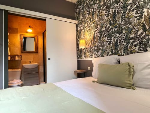 Chambre double cosy aux Maisons Delphine avec papier peint botanique, literie blanche et salle de bain attenante aux teintes orange chaleureuses