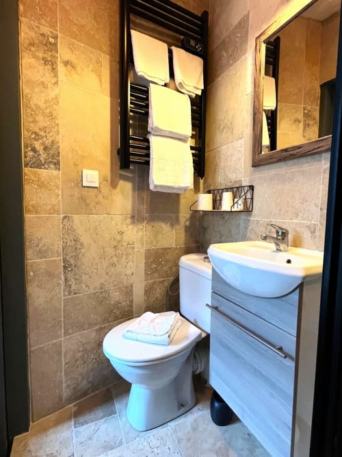 Salle de bain moderne aux Maisons Delphine Le Cottage avec vasque blanche, toilettes et murs en travertin à Villers-sur-Mer