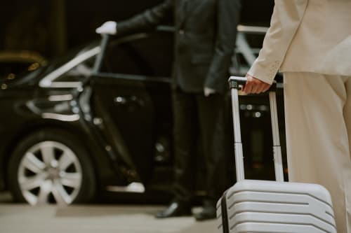 Guest holding luggage handle with car and driver in background at Hotel De Lion Sur Mer, France