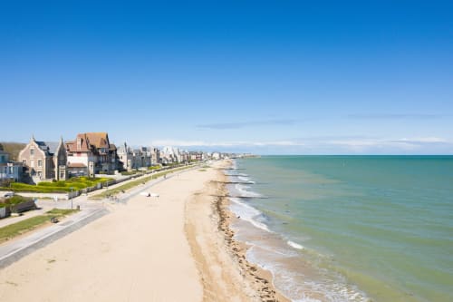 Beachfront Hotel De Lion Sur Mer with sandy shore, turquoise waters, and coastal buildings along the French Normandy coast