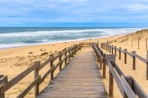 Wooden boardwalk leading to sandy beach with ocean waves at La Pause Landaise in Magescq, France