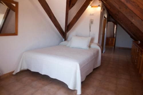 Acogedora habitación doble en buhardilla con vigas de madera vista, ropa de cama blanca y piso de madera oscura en Hostal Mar de Frente, Los Caños