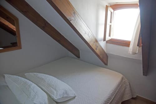 Habitación doble en buhardilla del Hostal Mar de Frente con vigas de madera, ropa de cama blanca y ventana en Los Caños de Meca