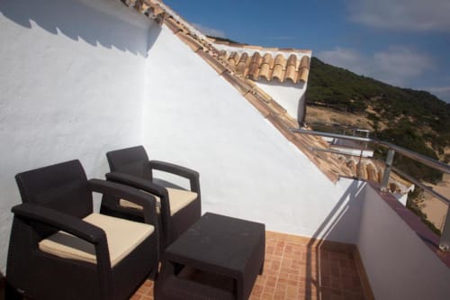 Cómodas sillas de mimbre con cojines en la terraza con vistas a la costa de Los Caños de Meca del Hostal Mar de Frente