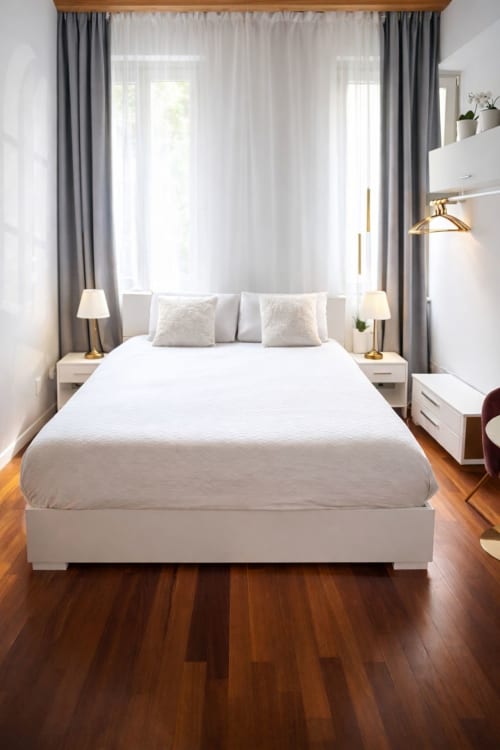 Camera da letto luminosa presso Lilia Luxury Suite Bergamo con letto bianco, tende grigie, pavimenti in legno e luce naturale