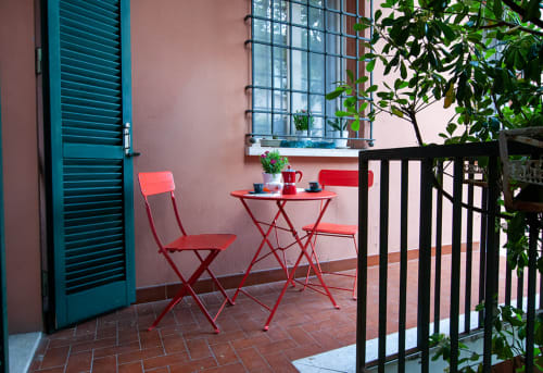 Cozy patio at Cristallo Apartment in Ravenna with red bistro furniture, teal shutters, and lush greenery