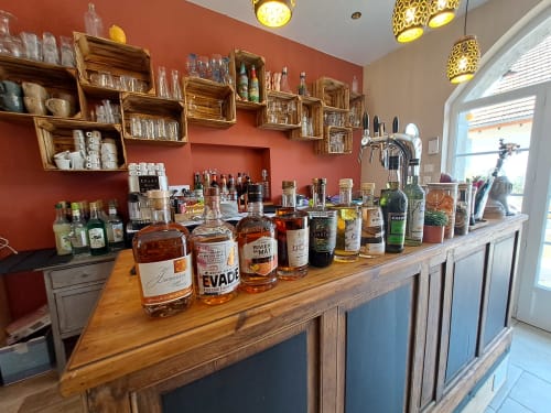 Bar counter at Clos De La Gourmandiere displaying spirits bottles, wooden shelves, and warm ambient lighting in Saint-Lothain