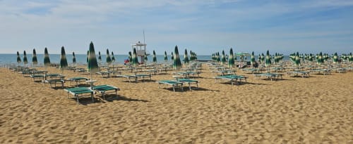 Strand von Jesolo mit ordentlichen Reihen grüner Sonnenschirme und Liegen, Rettungstürm und ruhige Adria