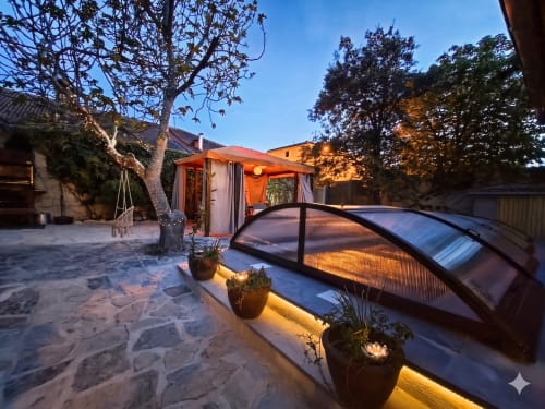 Vue nocturne du jardin du gîte Viento de Ladera à Ségovie avec patio illuminé, plantes en pot et bain à remous couvert