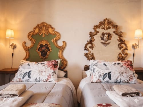 Deux lits jumeaux aux têtes de lit dorées ornementées dans une chambre de cottage à Ségovie avec coussins fleuris et appliques murales élégantes