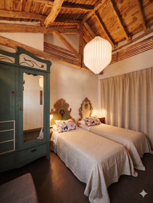 Lits jumeaux aux têtes de lit ornementées dans une chambre champêtre à Viento de Ladera, Ségovie, avec poutres apparentes