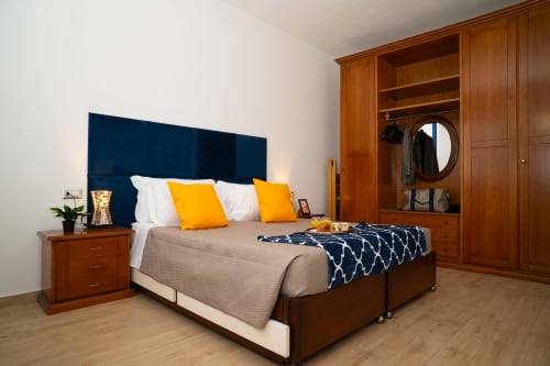 Camera da letto moderna con testata blu navy, cuscini gialli, mobili in legno e guardaroba nell'appartamento di Somma Lombardo