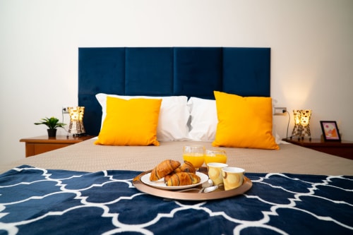 Camera da letto dell'appartamento Match Home Tramonto a Somma Lombardo con testata blu, cuscini gialli e vassoio colazione