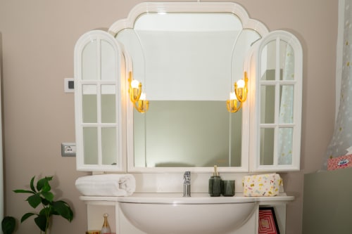 Elegante mobile bagno con cabinetry bianca, specchio arcuato, applique dorate e lavabo nell'appartamento Match Home a Somma Lombardo