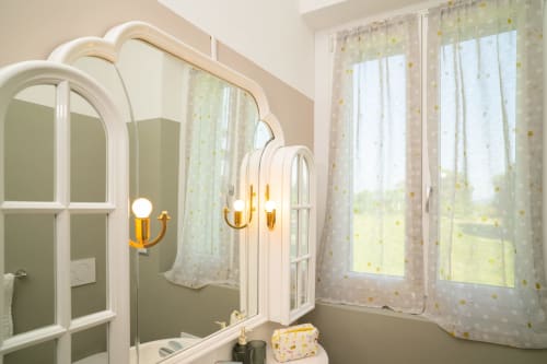 Bagno moderno con specchio ad arco bianco, finiture dorate e tende gialle trasparenti a motivi nell'appartamento Match Home