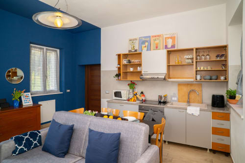 Cucina e zona living moderni con pareti blu, mobili in legno, dettagli arancioni e comodi sedili a Somma
