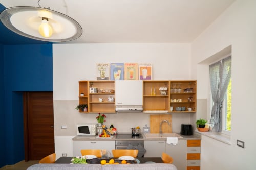 Cucina moderna con i suoi armadi in legno, gli elettrodomestici in acciaio inox e gli accenti arancioni nell'appartamento Tramonto di Match Home a Somma