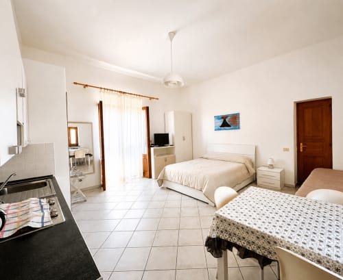 Ampio monolocale a Lipari con angolo cottura, due letti, pavimenti in piastrelle bianche e servizi moderni con aria condizionata e TV.
