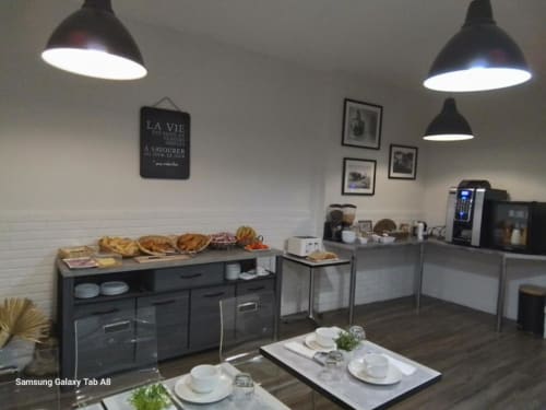 Salle de petit-déjeuner moderne à l'Hôtel le Vauban de Carentan avec suspensions noires, buffet garni et tables dressées
