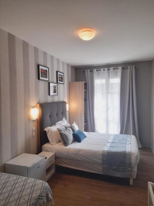 Chambre moderne à l'Hôtel le Vauban à Carentan avec papier peint rayé, lit tapissé gris et lumière naturelle des fenêtres